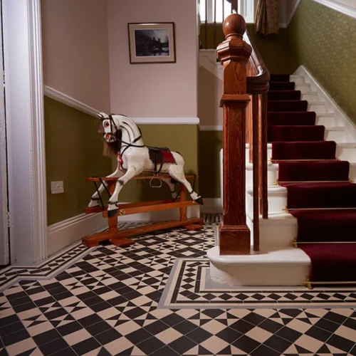 Black and white Braemar Victorian floor tile pattern with a Bronte border, installed in a traditional hallway with wooden staircase