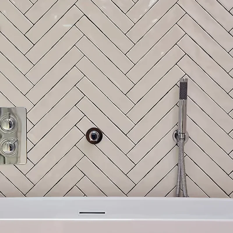 Avebury Plaster ceramic tile in a 25x5cm shown here as a herringbone wall behind a bath
