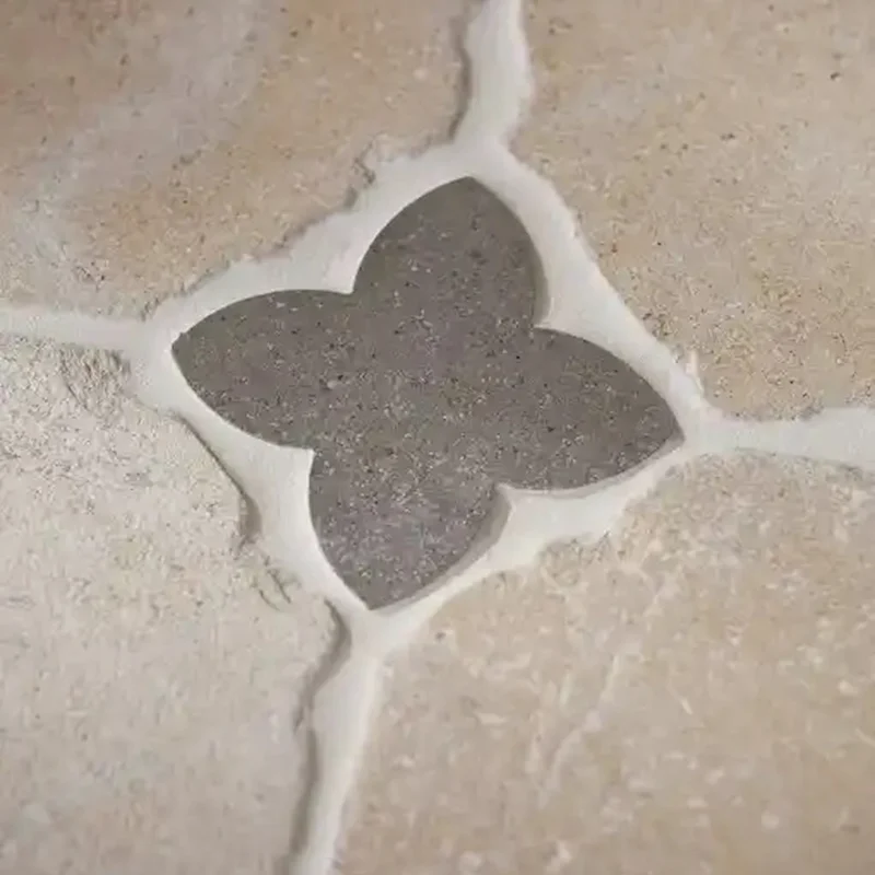 Beige stone floor tiles featuring a Hazlebury dark grey clover-shaped cabochon at the corner joints, adding a classic decorative touch.