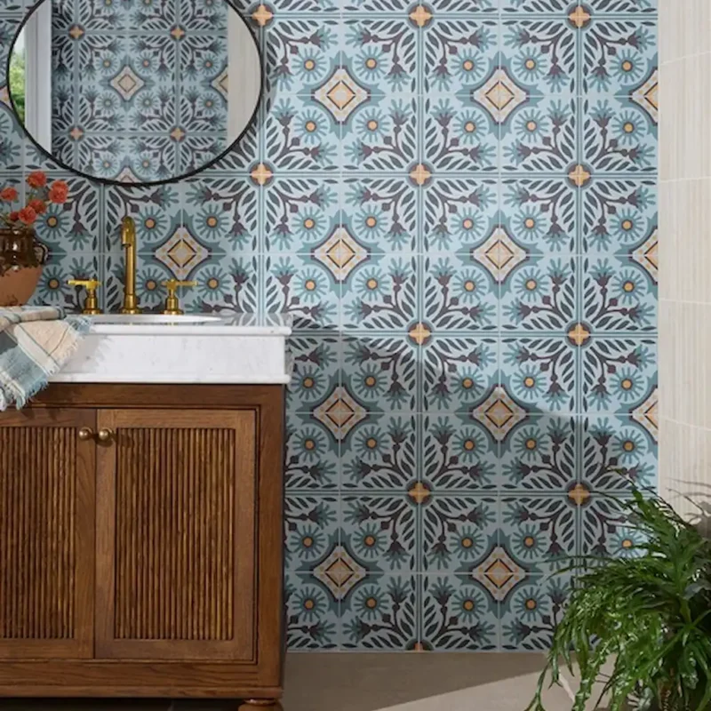 Indirah Porcelain Azure patterned wall tiles in a bathroom, featuring a soft blue geometric and floral design paired with a wooden vanity and brass tapware.