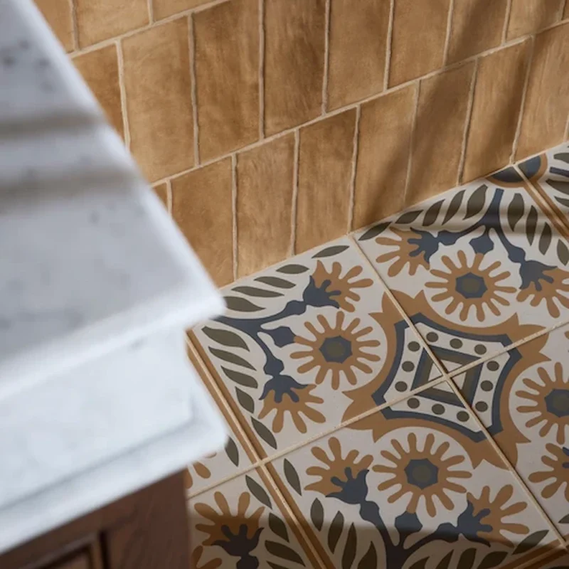 Close-up of Indirah Porcelain Cotto tiles showing a decorative geometric pattern in warm terracotta and muted blue tones, installed alongside wall tiles.