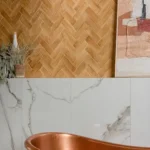 Oasis Veloute Ceramic Cotto Matt tiles in a warm herringbone layout, paired with marble-effect wall tiles and a freestanding copper bath