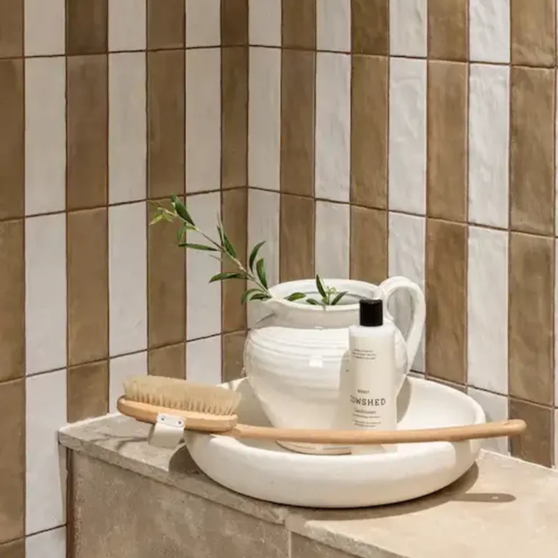 Oasis Veloute Ceramic Tan wall tiles with vertical stripes in tan and white, shown in a styled bathroom setting with natural accessories.