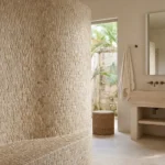 Enso Cobble Mosaic Strip Sand 30x32cm tile shown as a curved shower wall in warm neutral stone tones, natural pebble effect texture, spa-style bathroom setting