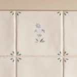 Close-up of Spring Alice Delft-style wall tiles showing delicate blue floral motif with green corner leaf pattern on gloss ceramic tiles.