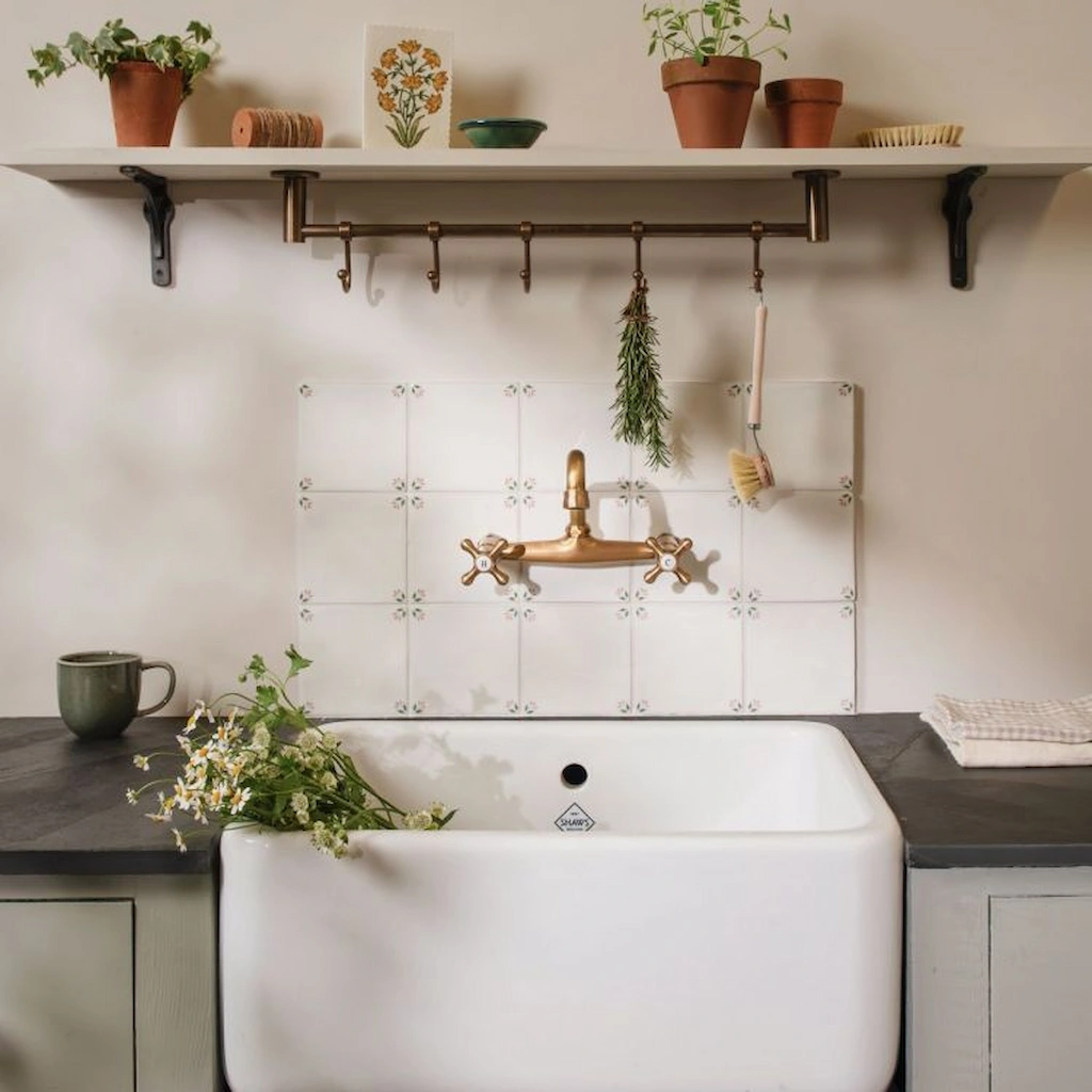 Spring April Blush Delft style tiles installed as a kitchen splashback with pink leaf corner pattern behind brass tap and ceramic sink