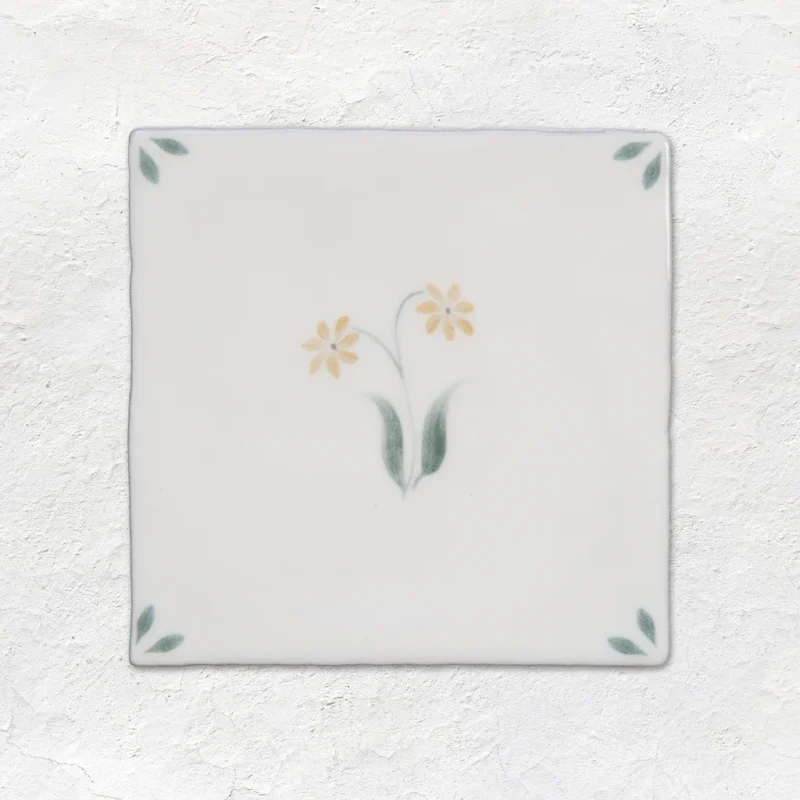 Spring Elsie Delft style tile 13x13cm with soft yellow floral design and green leaf corner detail on gloss off-white ceramic