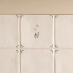 Spring Emma 13x13cm Delft style ceramic tile with delicate pink flower and green corner leaf details installed on a wall.