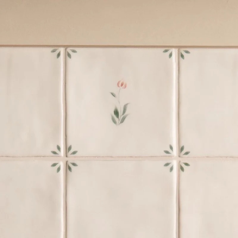 Spring Emma 13x13cm Delft style ceramic tile with delicate pink flower and green corner leaf details installed on a wall.