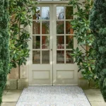 Tapestry Porcelain Paving Textured Arabic tile creating a soft patterned entrance pathway framed by greenery and traditional glazed doors.