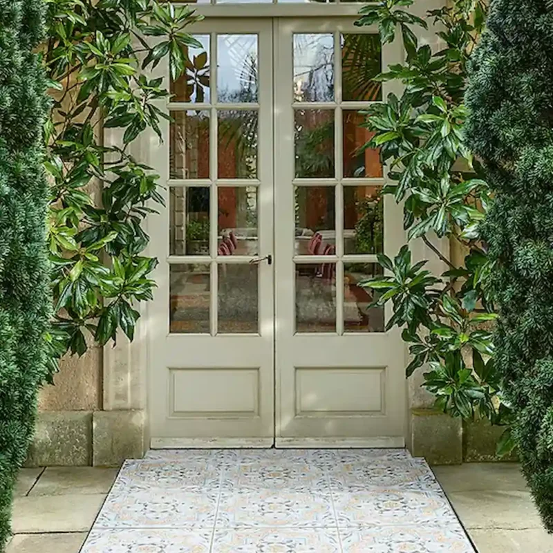 Tapestry Porcelain Paving Textured Arabic tile creating a soft patterned entrance pathway framed by greenery and traditional glazed doors.